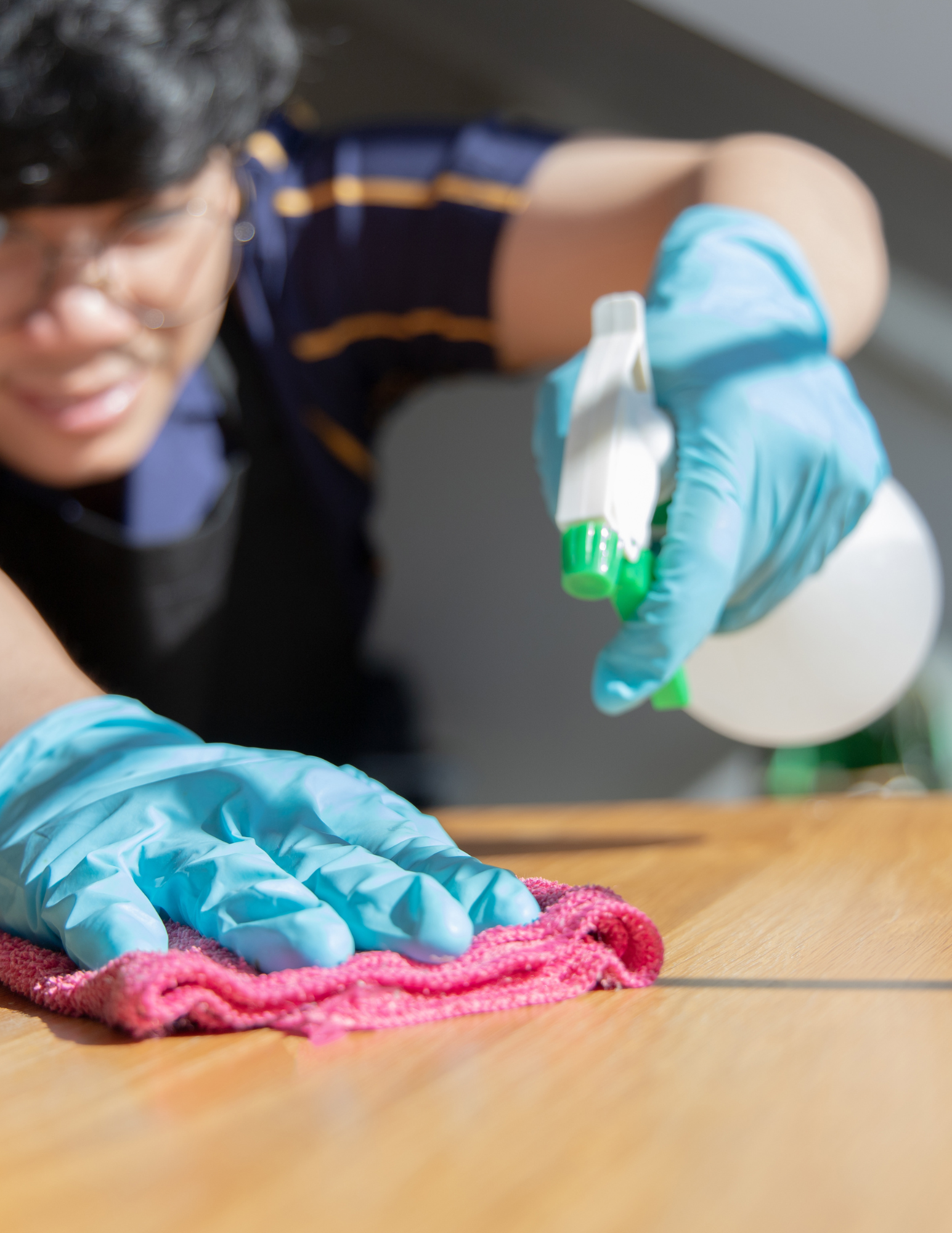 Cleaner spraying and wiping a table with a microfiber cloth